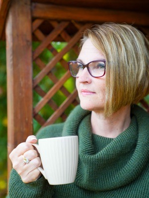 Anna holding a mug of coffee looking thoughtfully into the distance